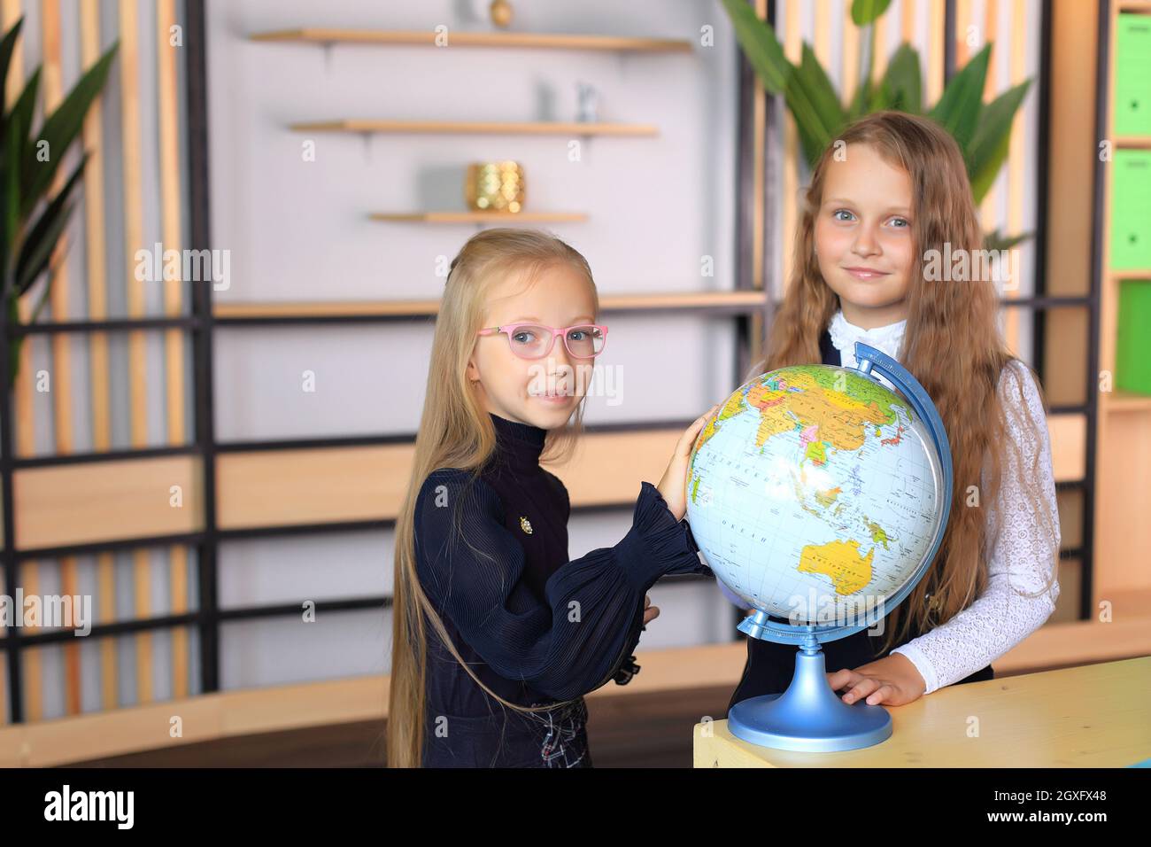 Children in school uniforms with a globe in the office. Girls in the school class. Portraits of schoolgirls in a geography lesson Stock Photo