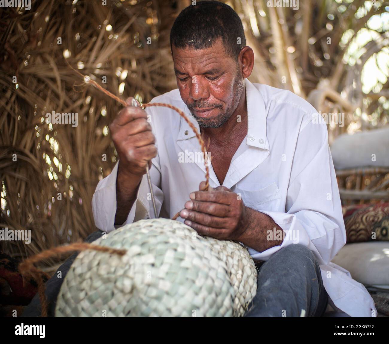 A Siwan man is weaving palm leaf into traditional bags and mat. The traditional straw plaited bags are still used widely in Siwa Oasis. Stock Photo