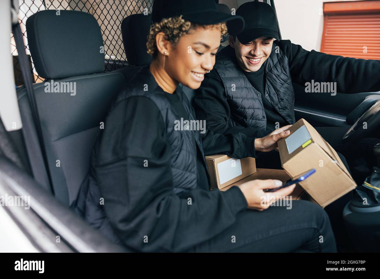 Two couriers sitting in car checking information on box using mobile phone Stock Photo