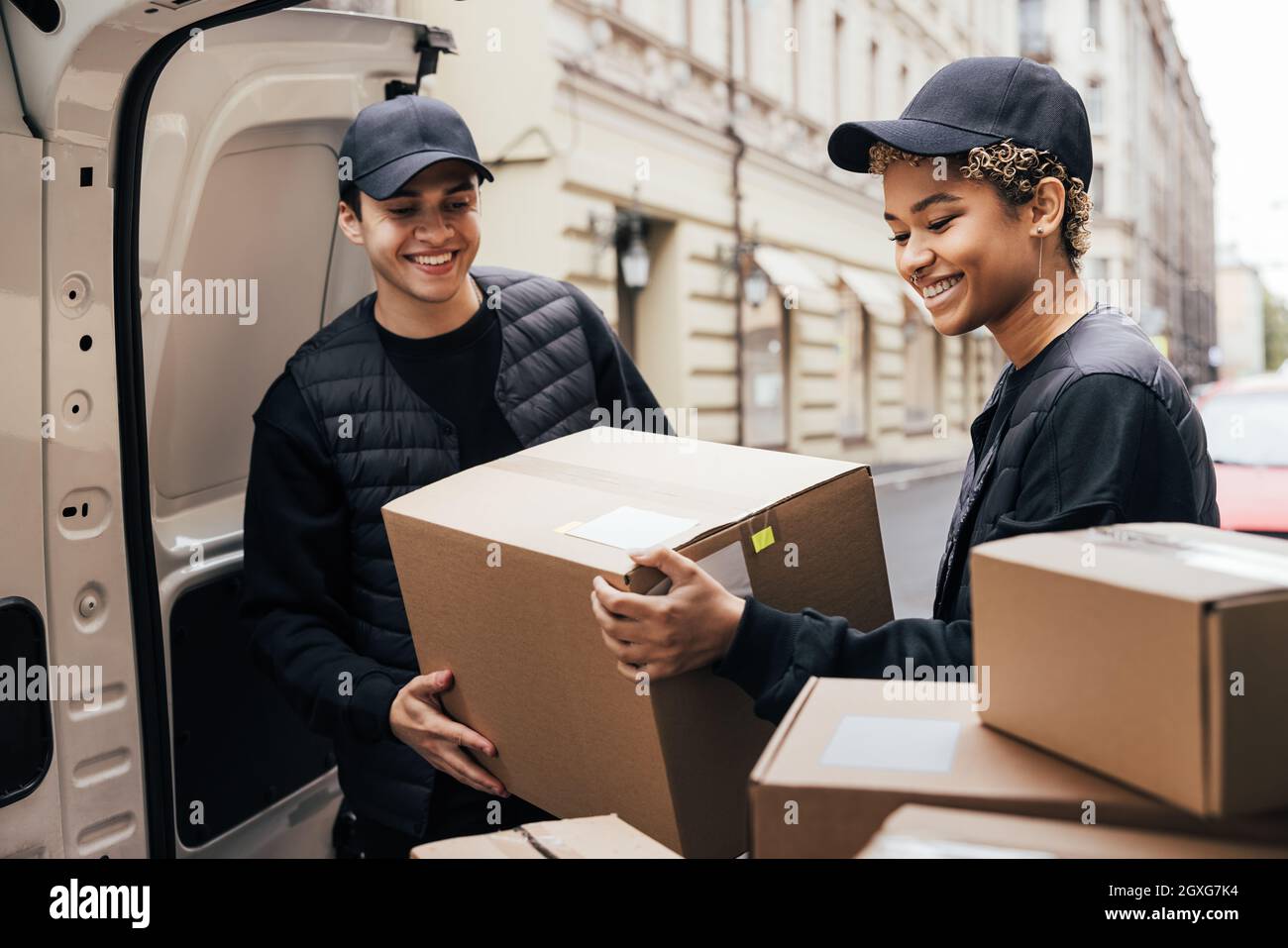 Two smiling couriers unloading cardboard boxes from van in the city Stock Photo