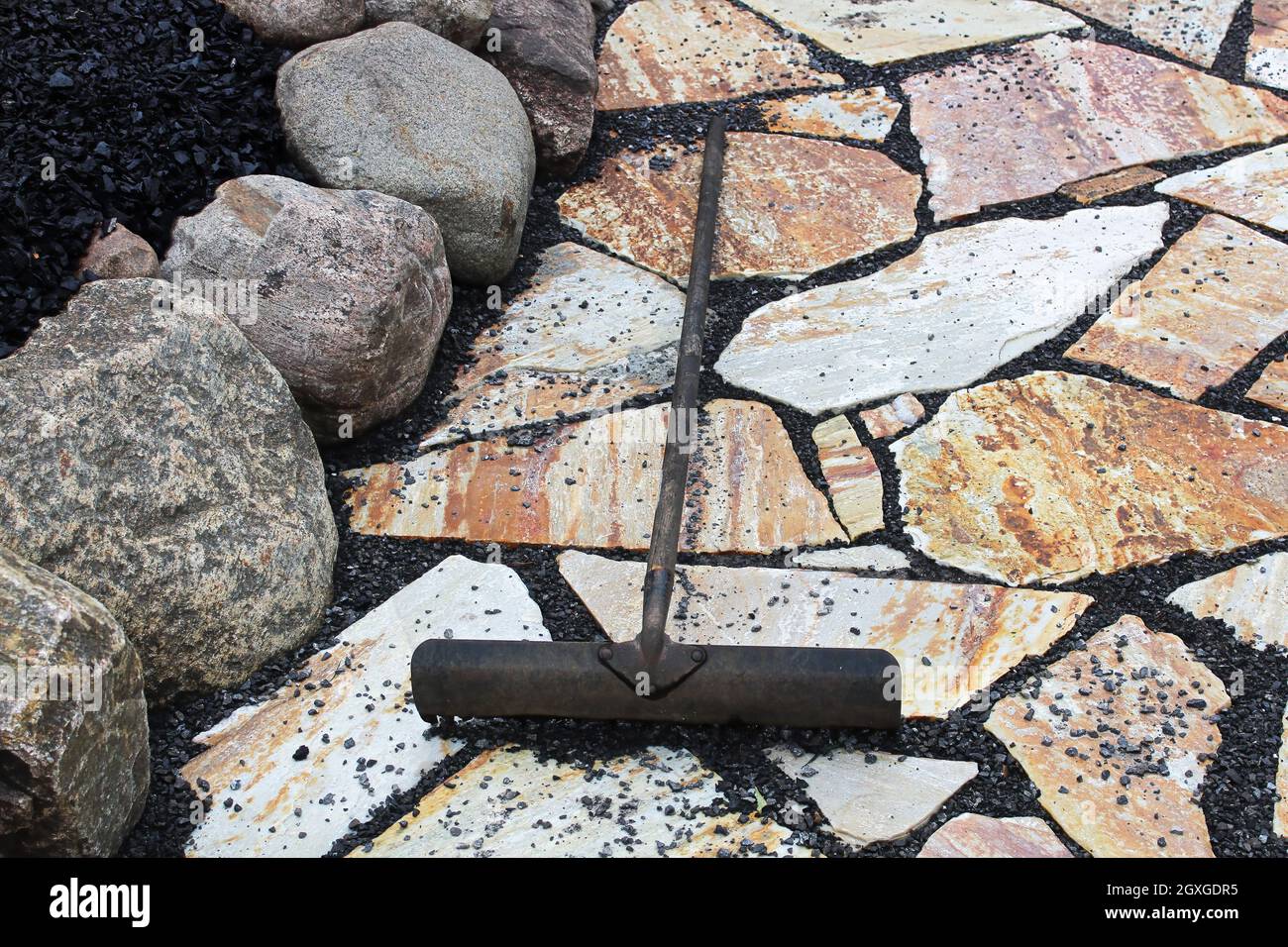 A rake being used to place black pebbles between patio stones Stock