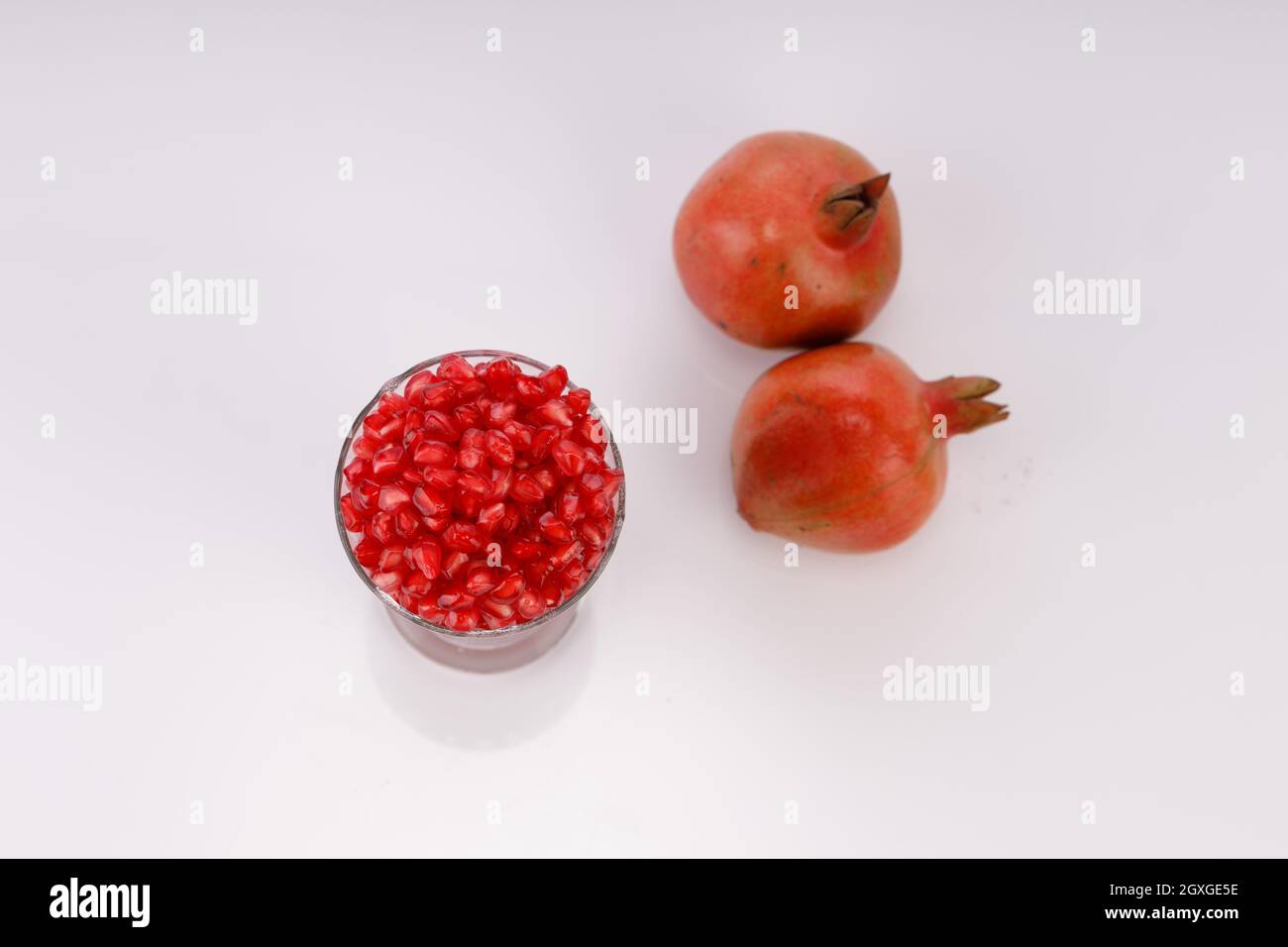 Fresh Pomegranate seed arranged in a glass container with fresh fruit placed beside it on white background, isolated. Stock Photo