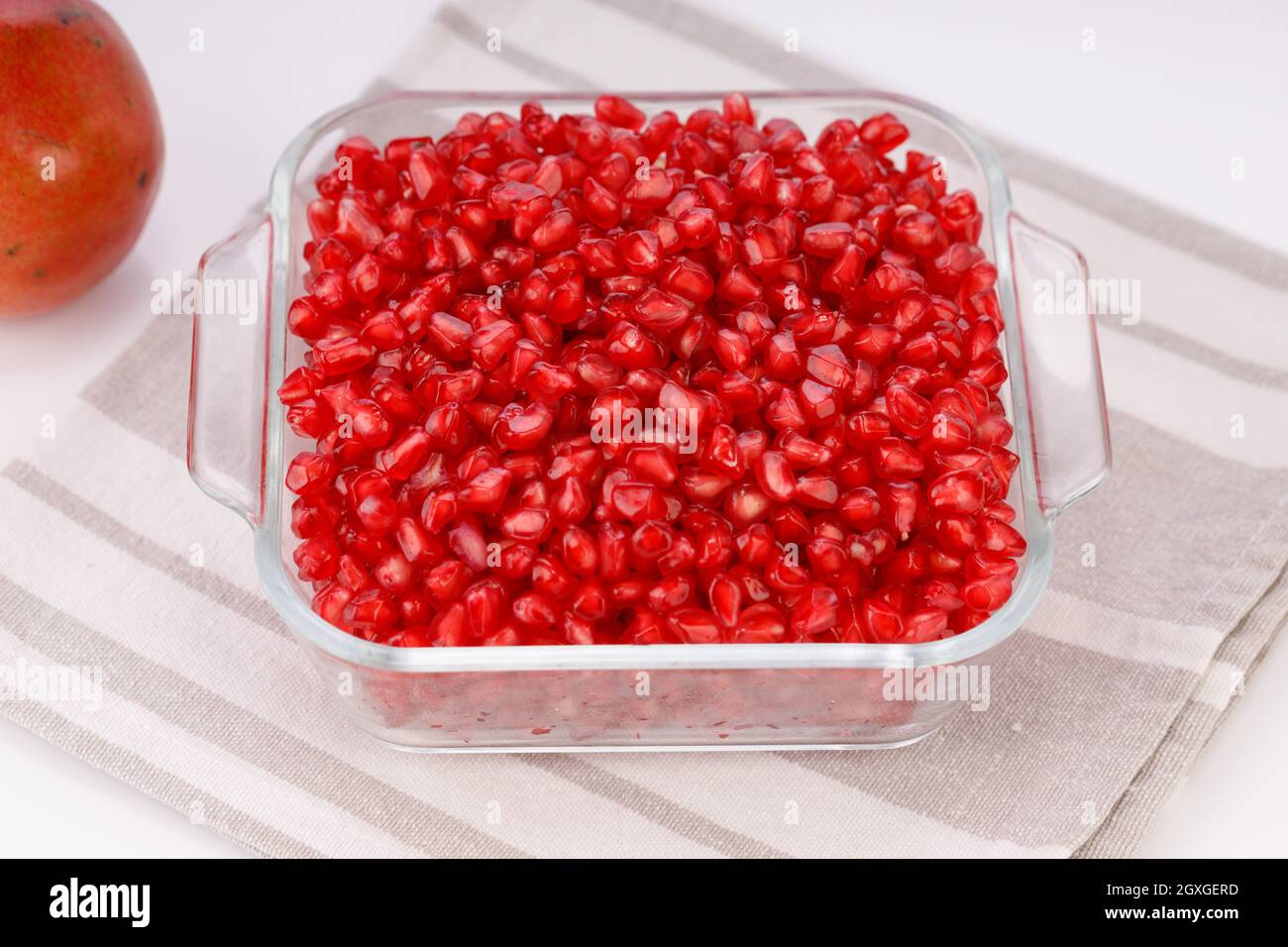 Fresh Pomegranate seed arranged in a square glass container with fresh fruit placed beside it on white background, isolated. Stock Photo