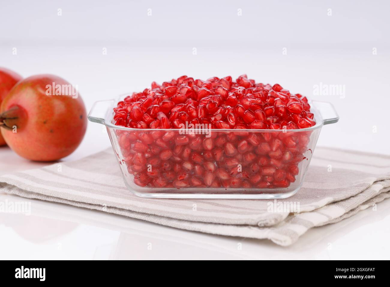 Fresh Pomegranate seed arranged in a square glass container with fresh fruit placed beside it on white background, isolated. Stock Photo