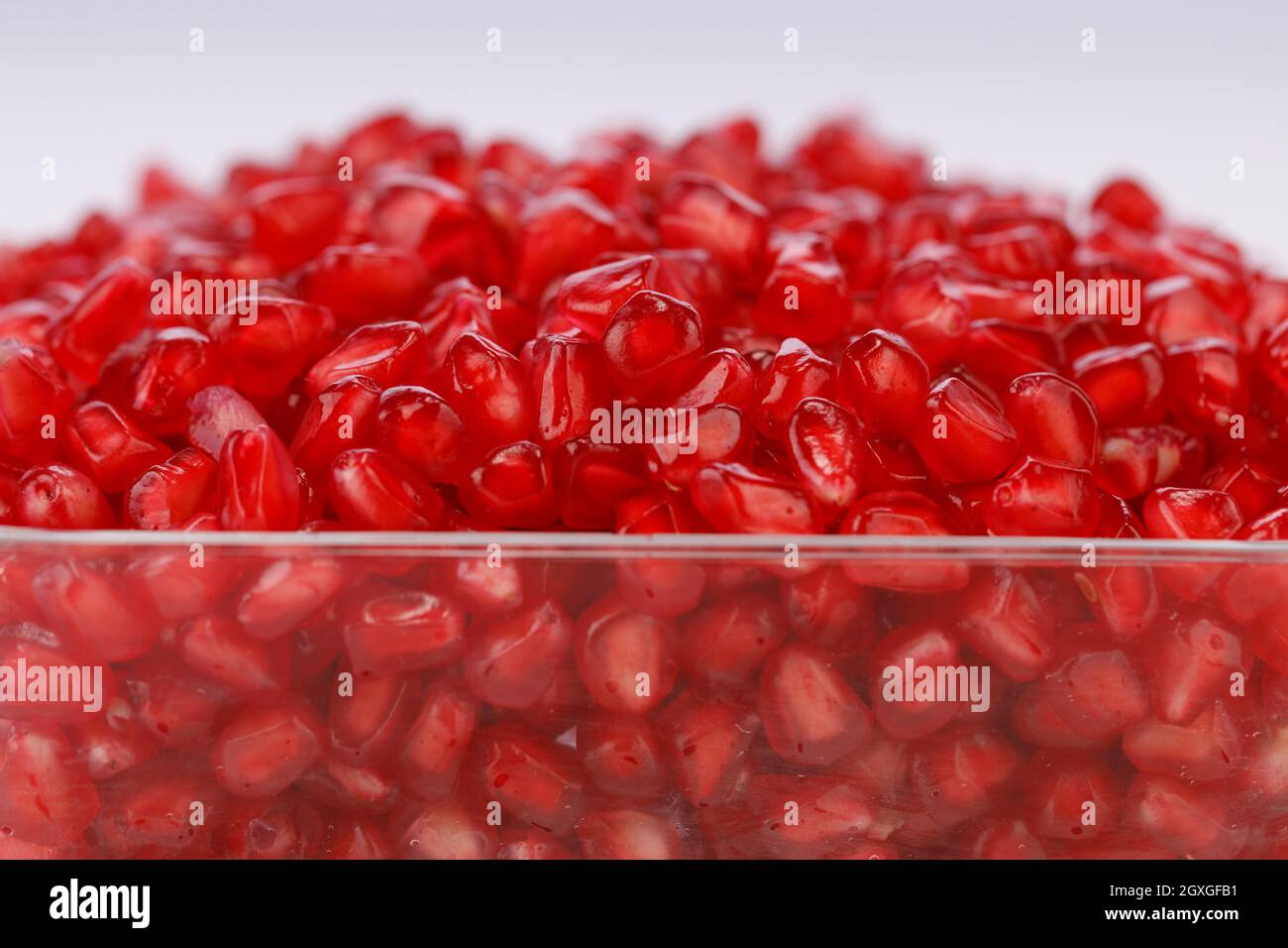 Fresh Pomegranate seed arranged in a square glass container with white background, isolated, close up. Stock Photo