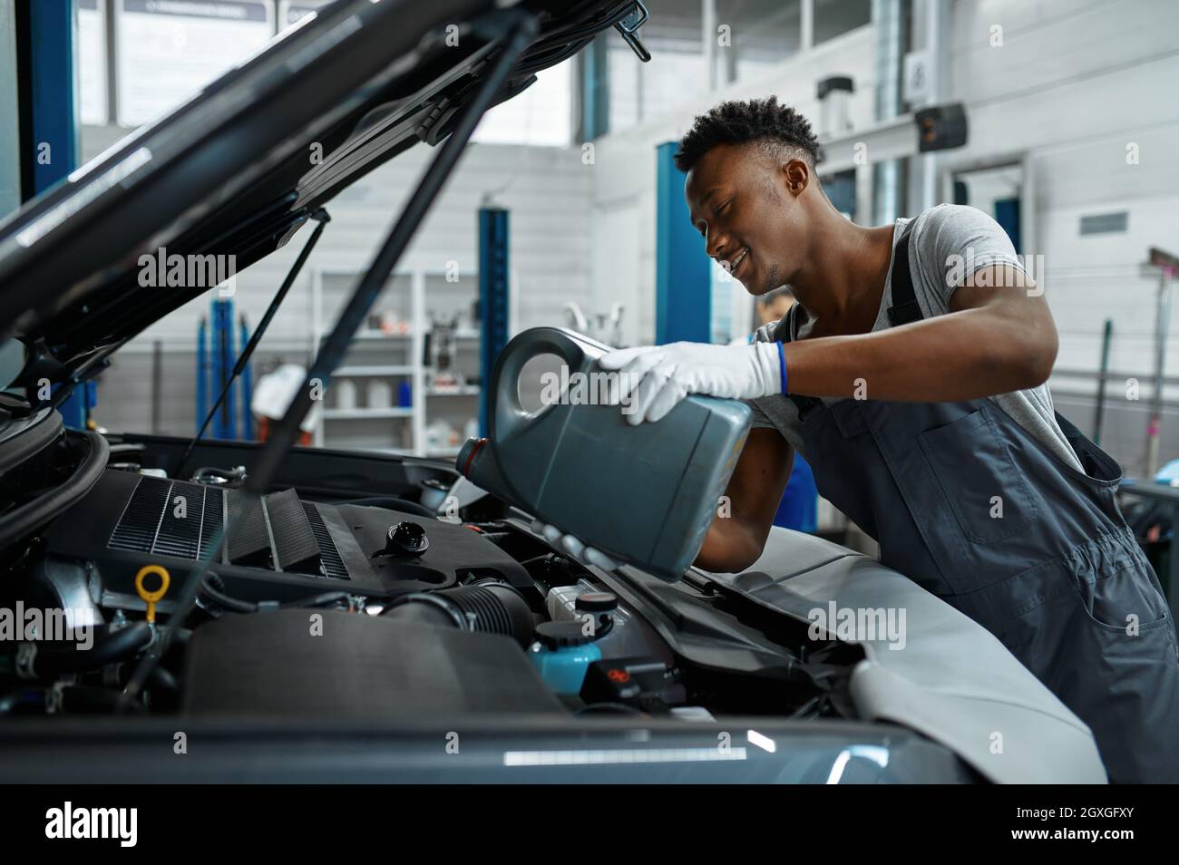 Male worker changes oil in engine, car service. Vehicle repairing