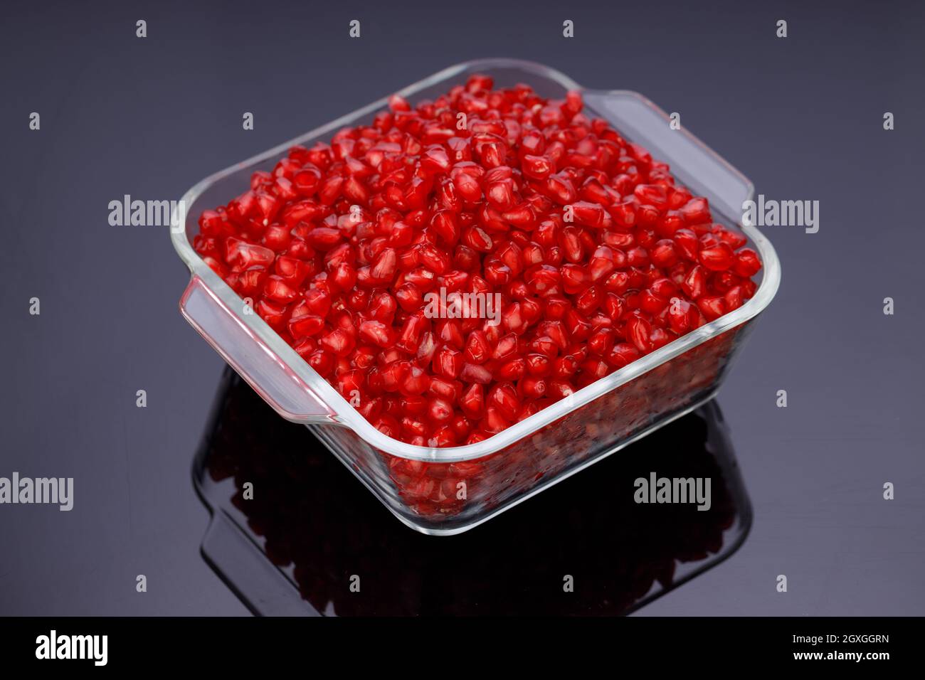 Fresh Pomegranate seed arranged in a square glass container on black background, isolated. Stock Photo