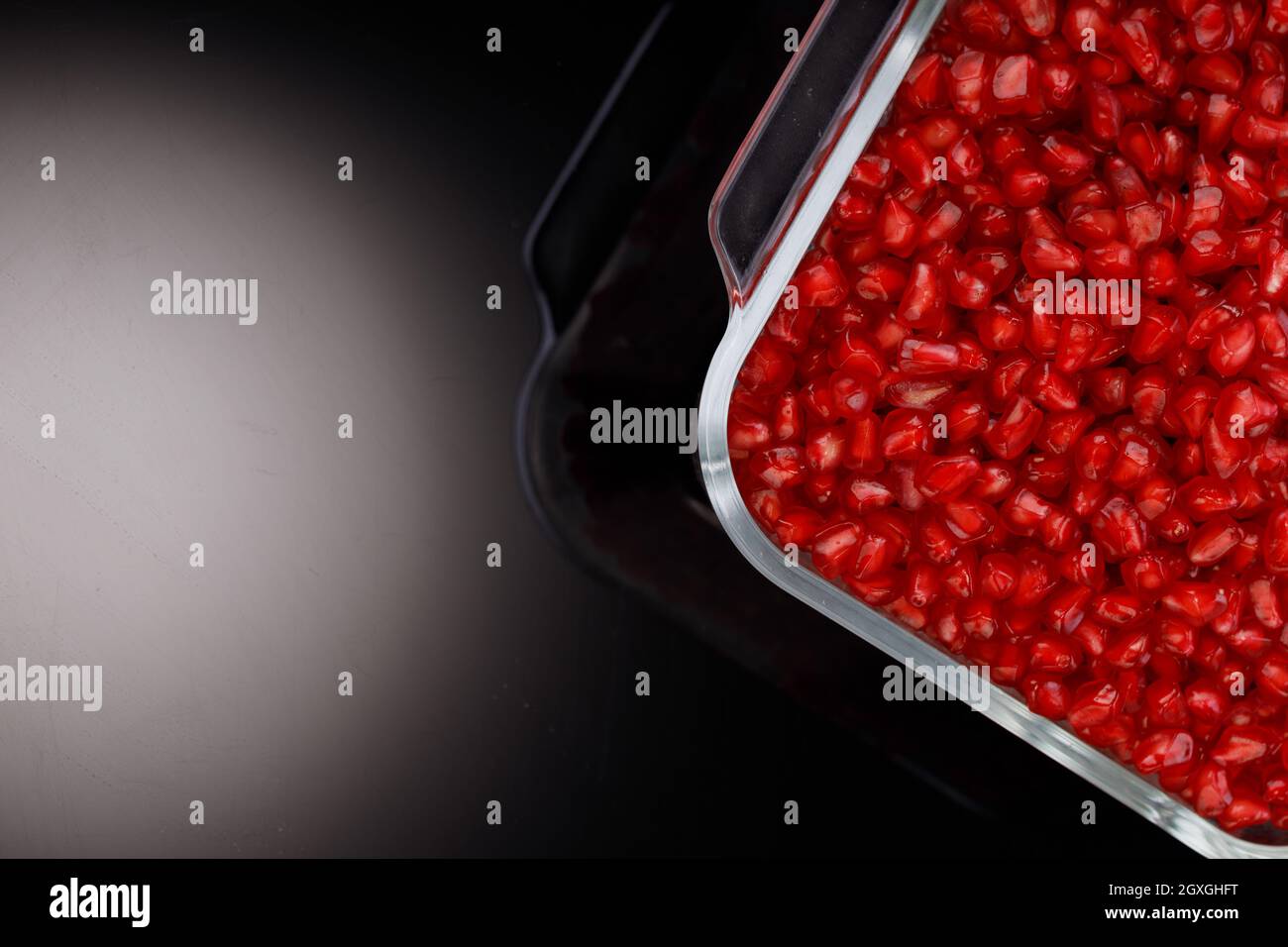Fresh Pomegranate seed arranged in a square glass container with fresh fruit placed beside it on grey background, isolated. Stock Photo
