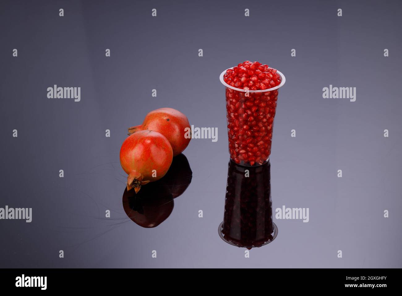 Fresh Pomegranate seed arranged in a  glass  with fresh fruit placed beside it on grey background, isolated. Stock Photo