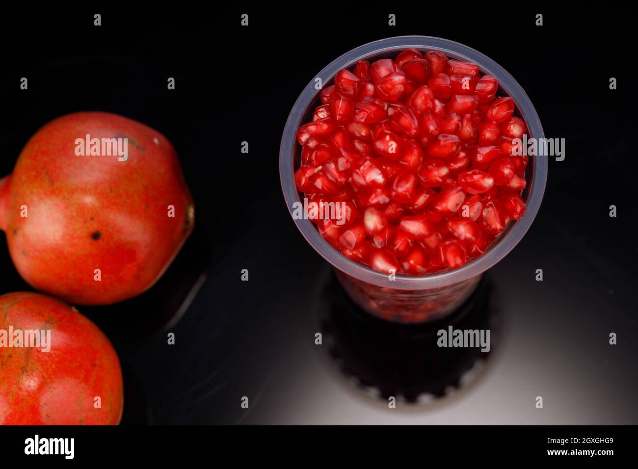 Fresh Pomegranate seed arranged in a  glass  with fresh fruit placed beside it on grey background, isolated. Stock Photo