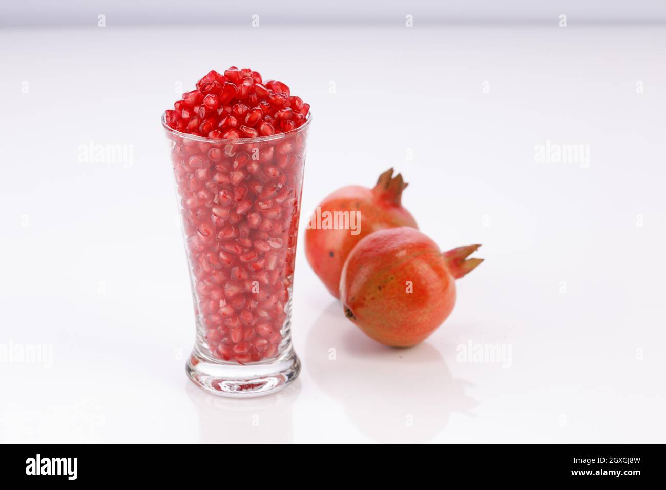 Fresh Pomegranate seed arranged in a glass container with fresh fruit placed beside it on white background, isolated. Stock Photo