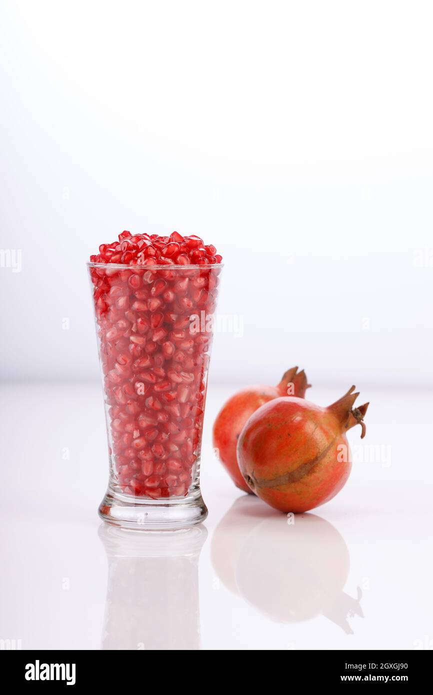 Fresh Pomegranate seed arranged in a glass container with fresh fruit placed beside it on white background, isolated. Stock Photo