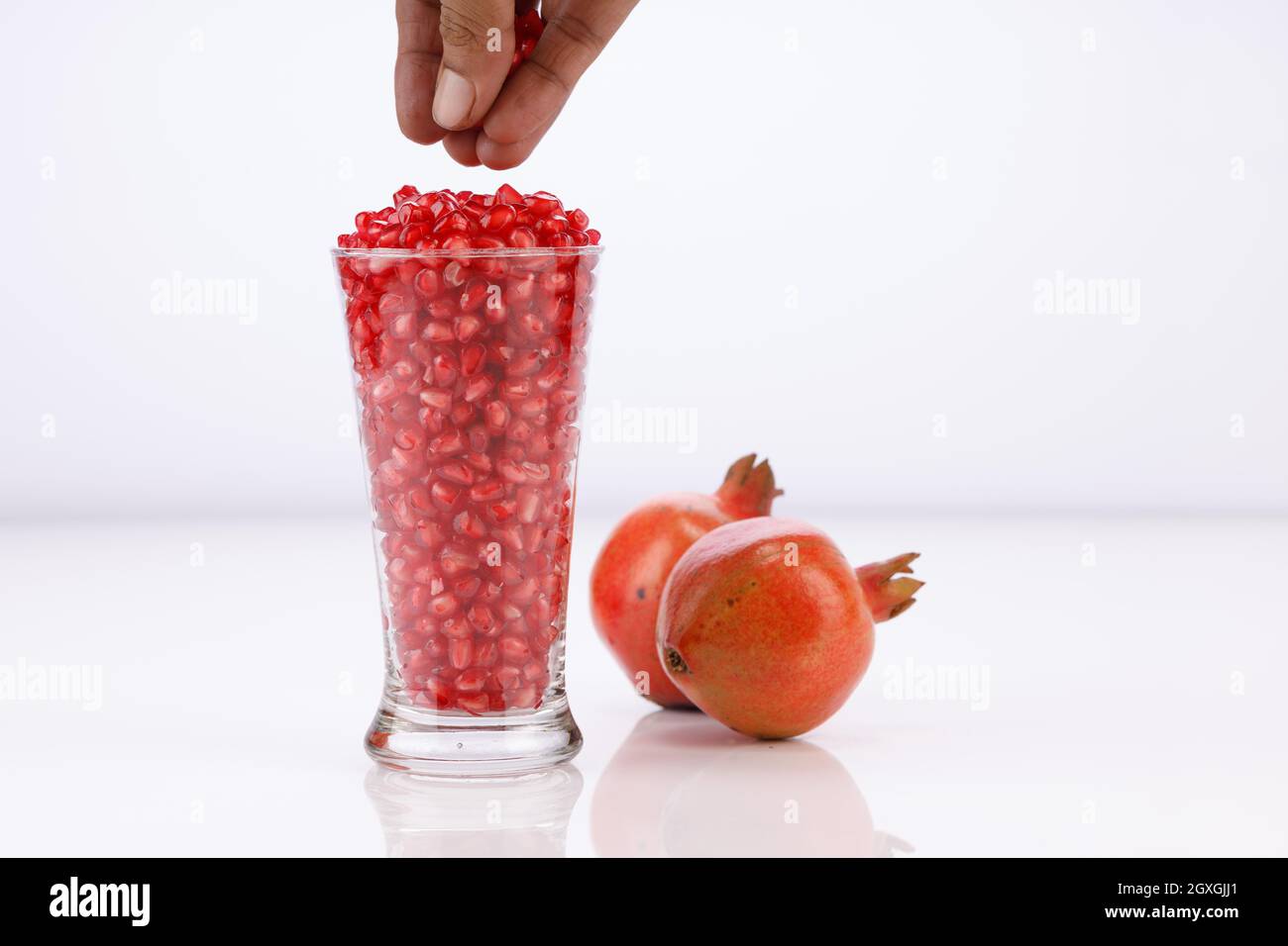 Fresh Pomegranate seed arranged in a glass container with fresh fruit placed beside it on white background, isolated. Stock Photo