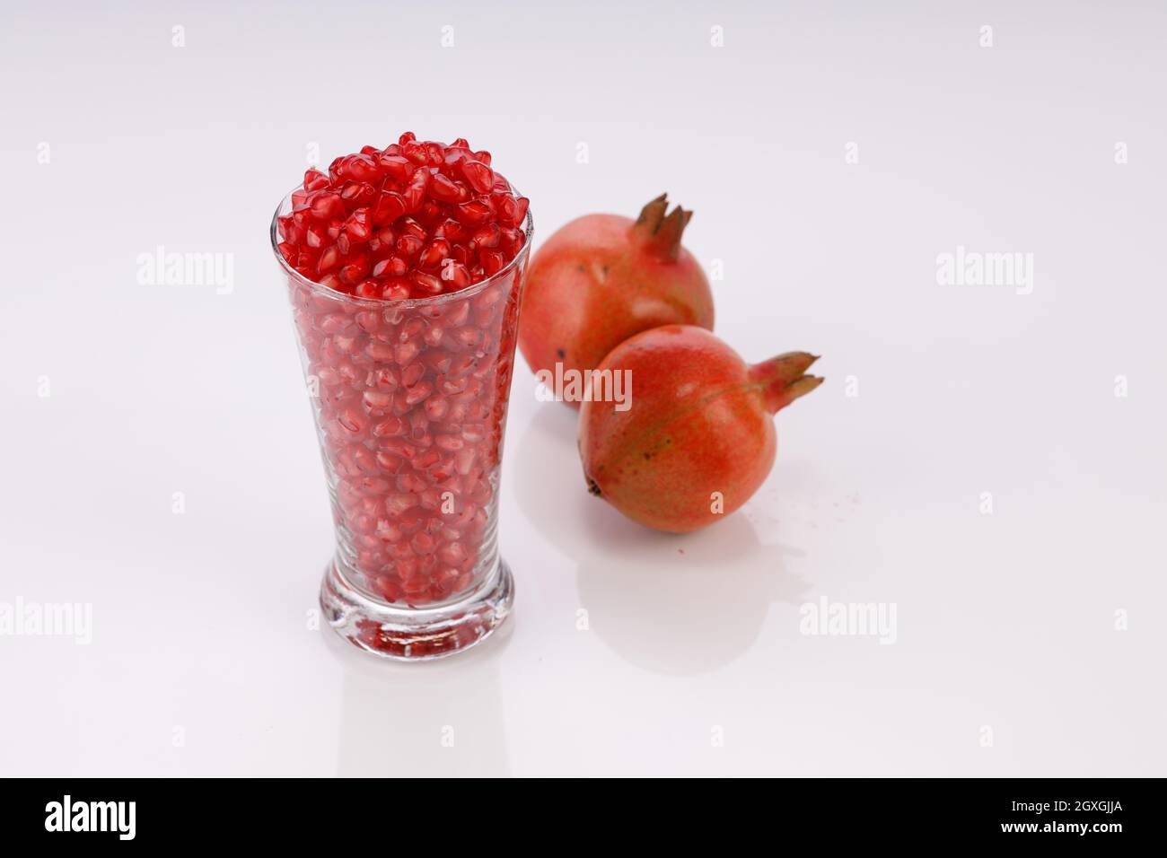 Fresh Pomegranate seed arranged in a glass container with fresh fruit placed beside it on white background, isolated. Stock Photo