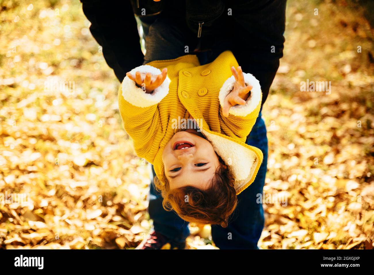 Happy little girl in yellow jacket playing with her father in park. Child smiling and hanging in autumn forest. Family time fun in autumn season. Stock Photo