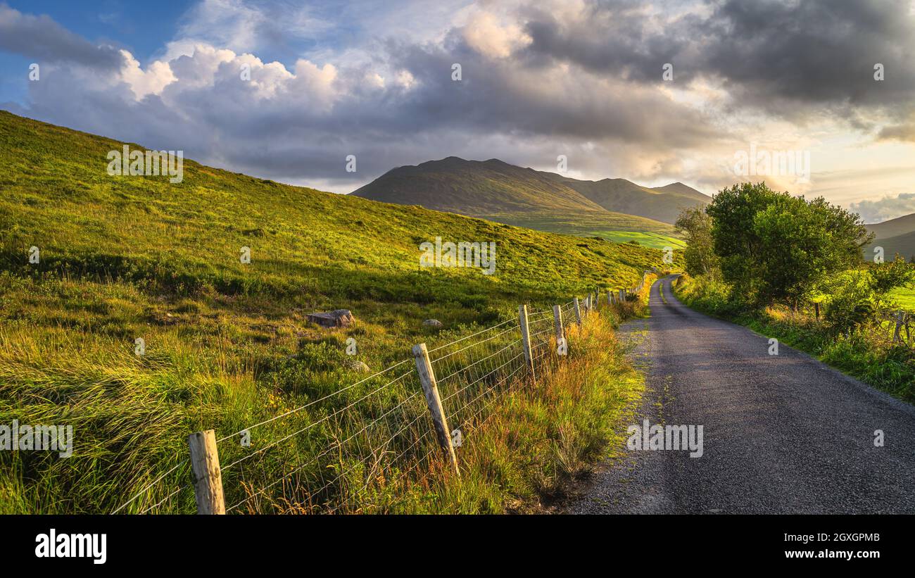 Winding country road leading toward highest mountain in Ireland, Carrauntoohil in MacGillycuddys Reeks mountains at sunset, Ring of Kerry, Ireland Stock Photo