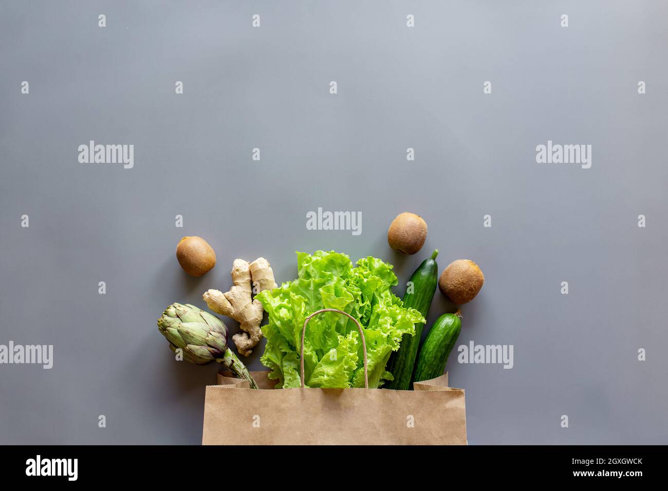 Healthy and organic food flay lay concept on gray background. Eco bag with scattered lettuce salad leaves, kiwi, kiwi, cucumber, artichoke and ginger Stock Photo