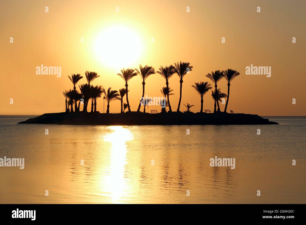 Beautiful place for privacy. Sunset over island in sea. Bright sun during dawn over the sea. Island with palm trees and benches in ocean. Summer vacat Stock Photo