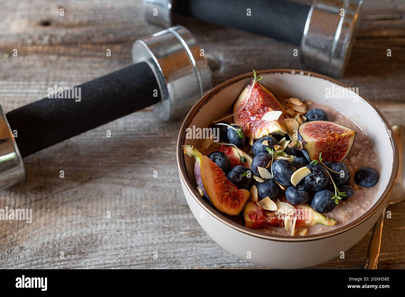 Fitness breakfast bowl with a delicious porridge cooked with chocolate whey protein powder and served with fruits and roasted almonds on wooden table Stock Photo