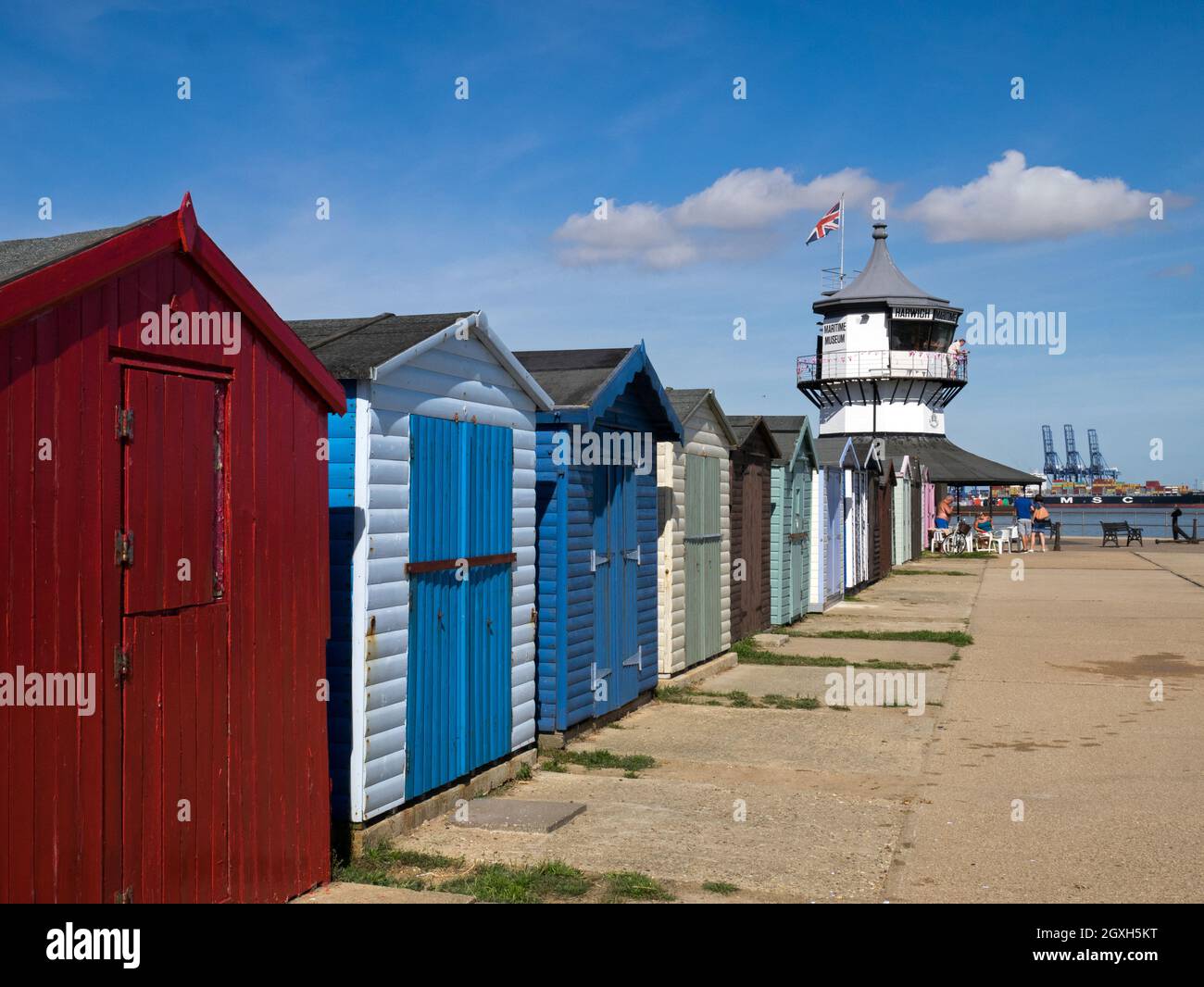 Row of Colourful Beach Huts with Harwich Low Lighthouse, Maritime Museum, & Felixstowe Container Port distance, Harwich, Essex,  England, UK Stock Photo