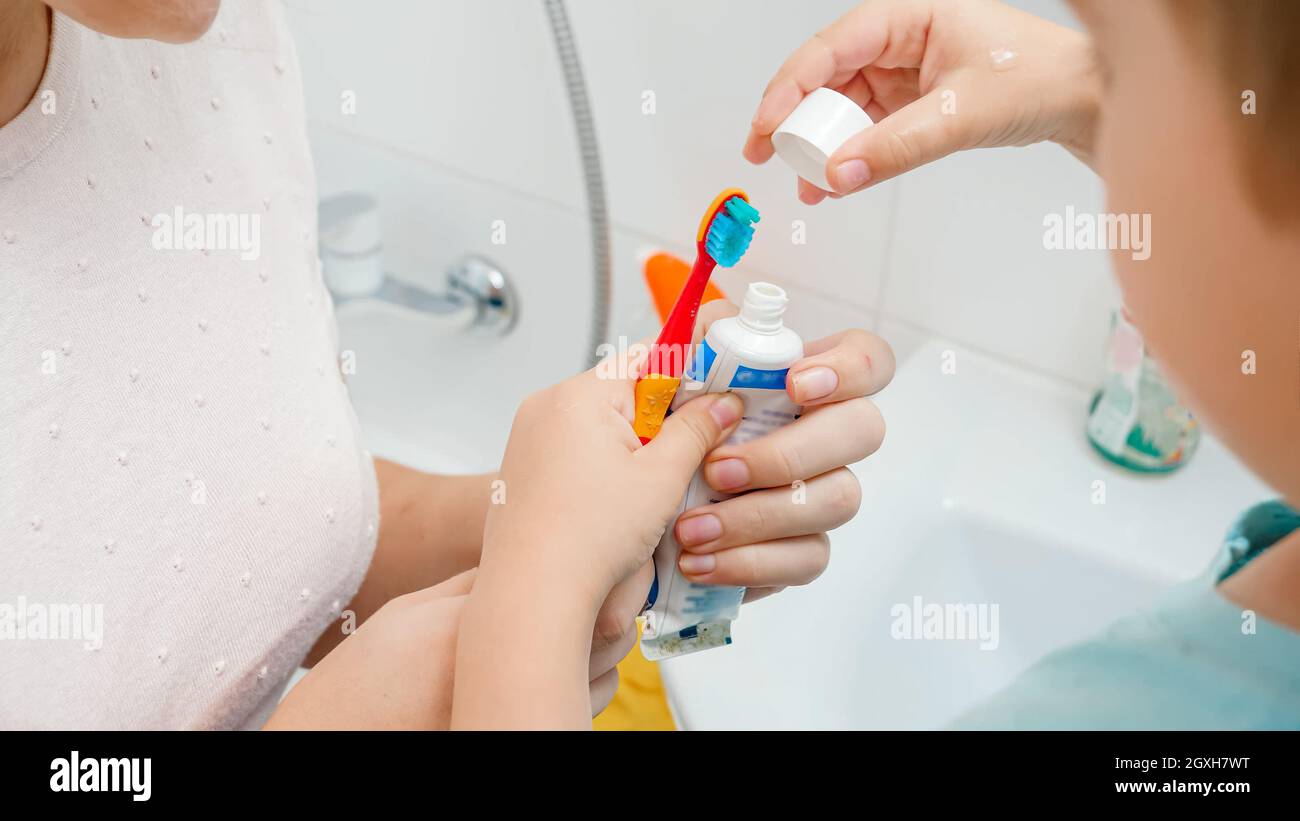 Closeup of mother helping her toddler son applying tooth paste. Child using toothbrush and toothpaste for brushing and cleaning teeth. Stock Photo