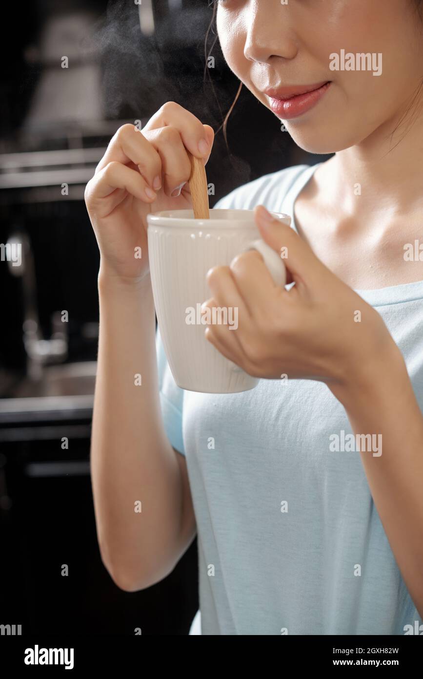 Close-up of content Asian girl stirrign sugar with spoon and smelling coffee scent in kitchen Stock Photo