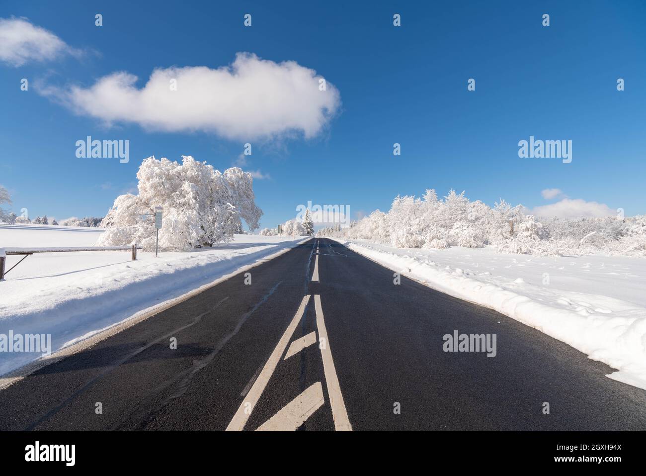 An empty road in winter leading through the mountains of Rhön and a lanscape of snow and ice covered trees and meadows with beautiful blue sky and sun Stock Photo