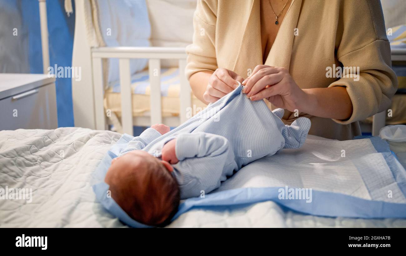 Closeup of young woman dressing her newborn baby boy in new clean and