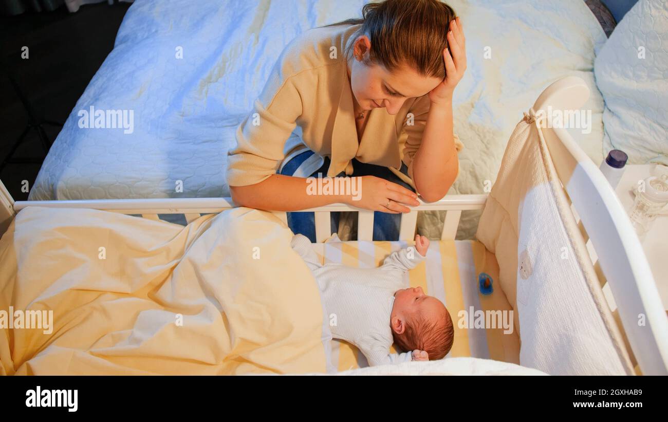 Exhausted young woman rocking crib of her sleepless newborn baby