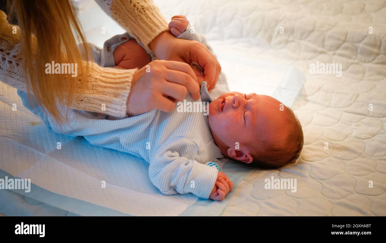 Top view of mother dressing her little newborn baby on bed at night