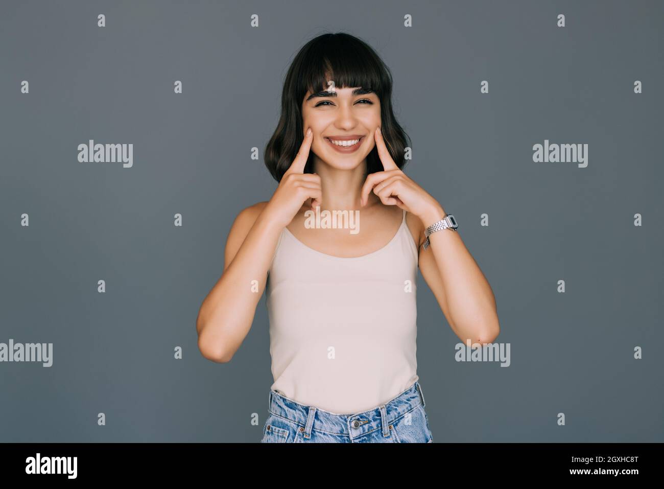 Clean and healthy teeth. Young smiling beautiful woman i points fingers to her teeth on a gray background Stock Photo