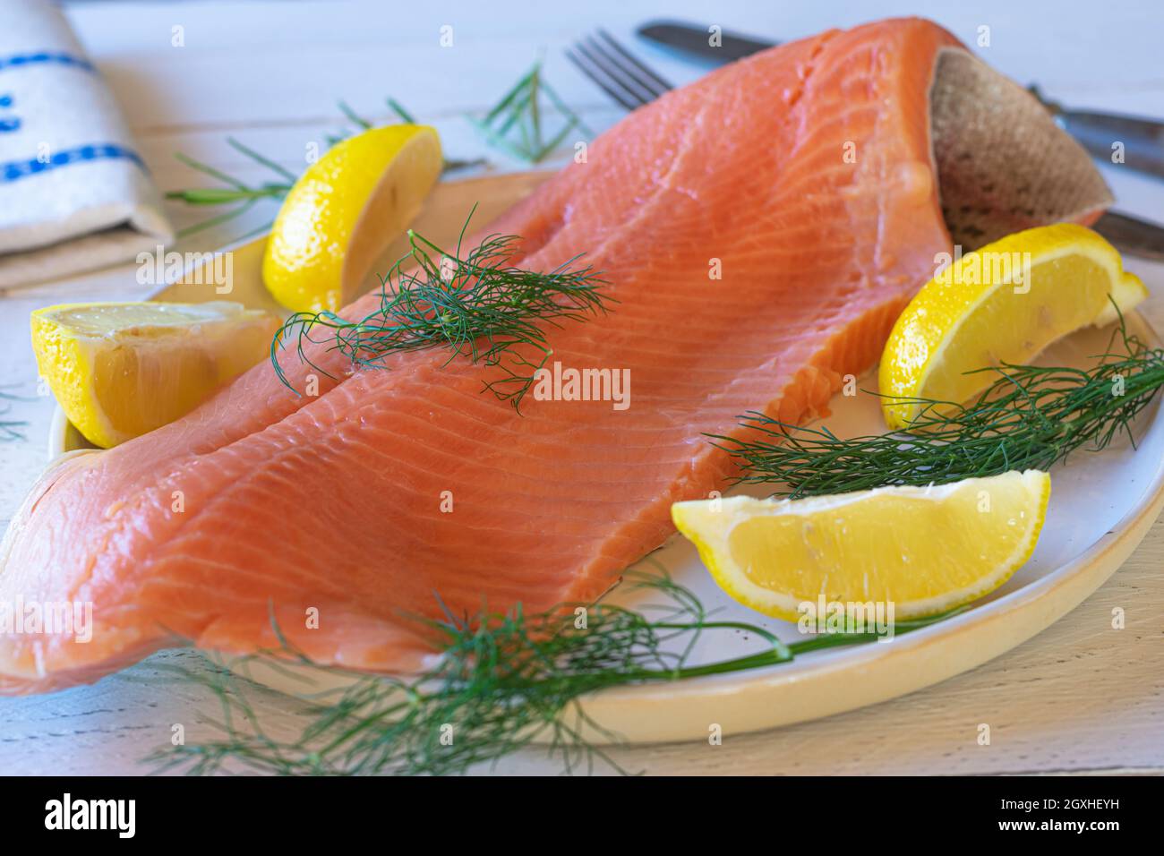 Raw and uncooked half salmon fillet on white background with lemon and dill. Fish with skin