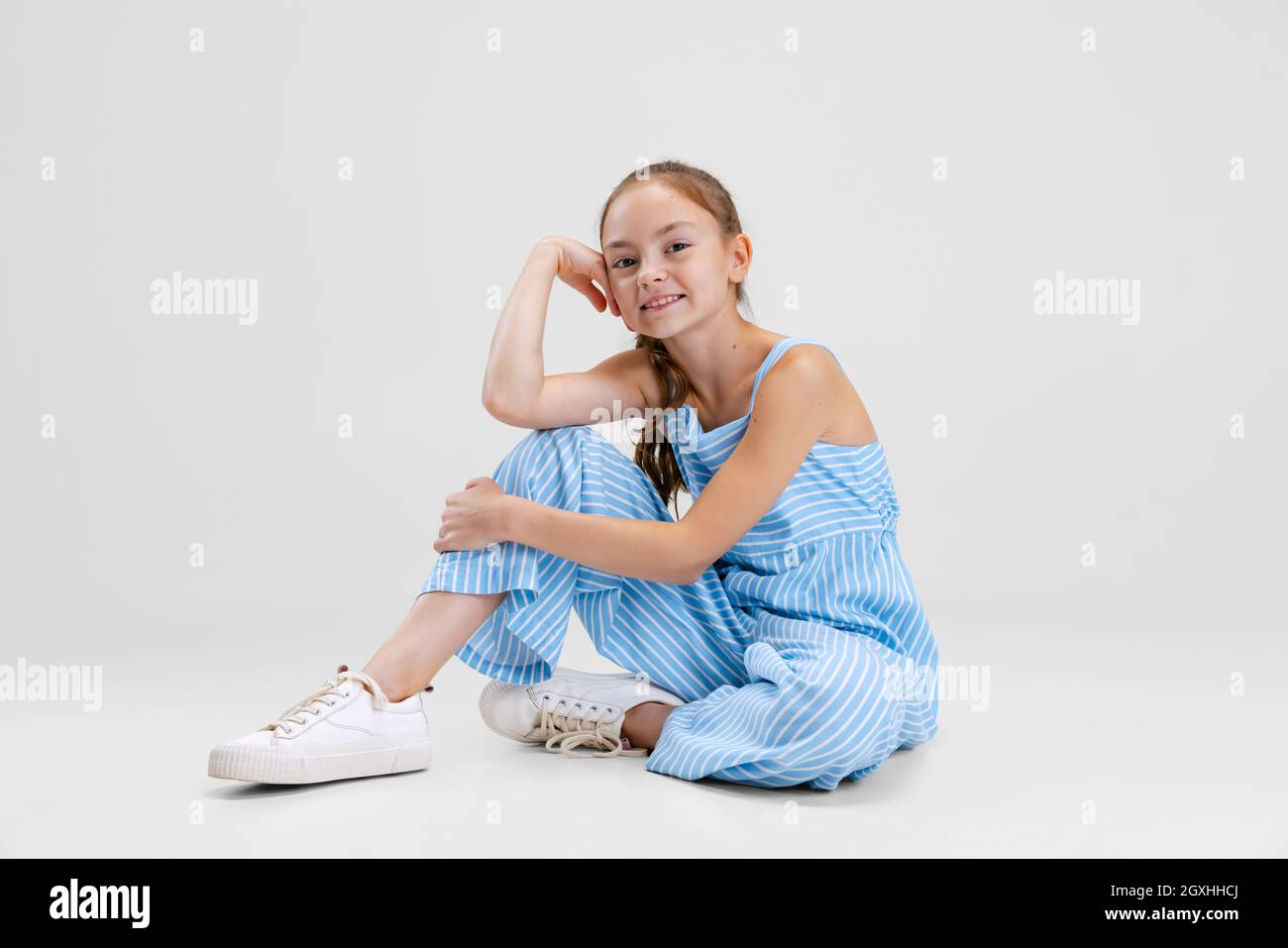Portrait of little Caucasian cute girl calmly sitting and smiling isolated over gray studio
