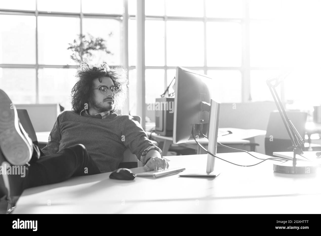 Full length of a relaxed casual young businessman sitting with legs on desk at office Stock Photo