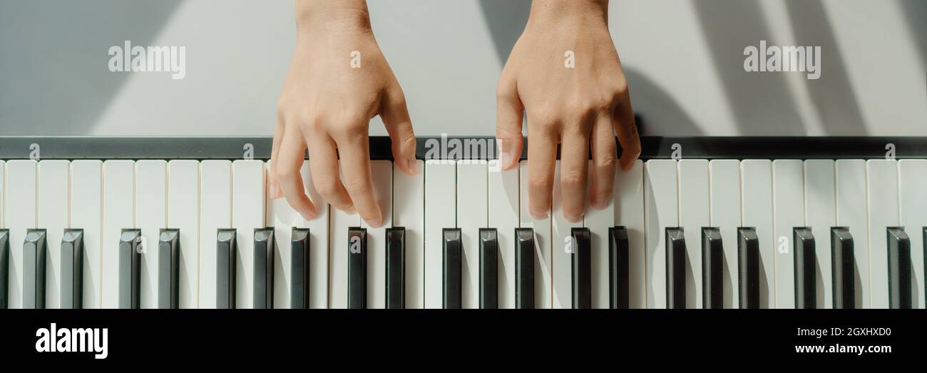 Woman learning to play piano at home on digital keyboard. Panoramic banner crop of hands playing beginner chords to learn playing by herself Stock Photo