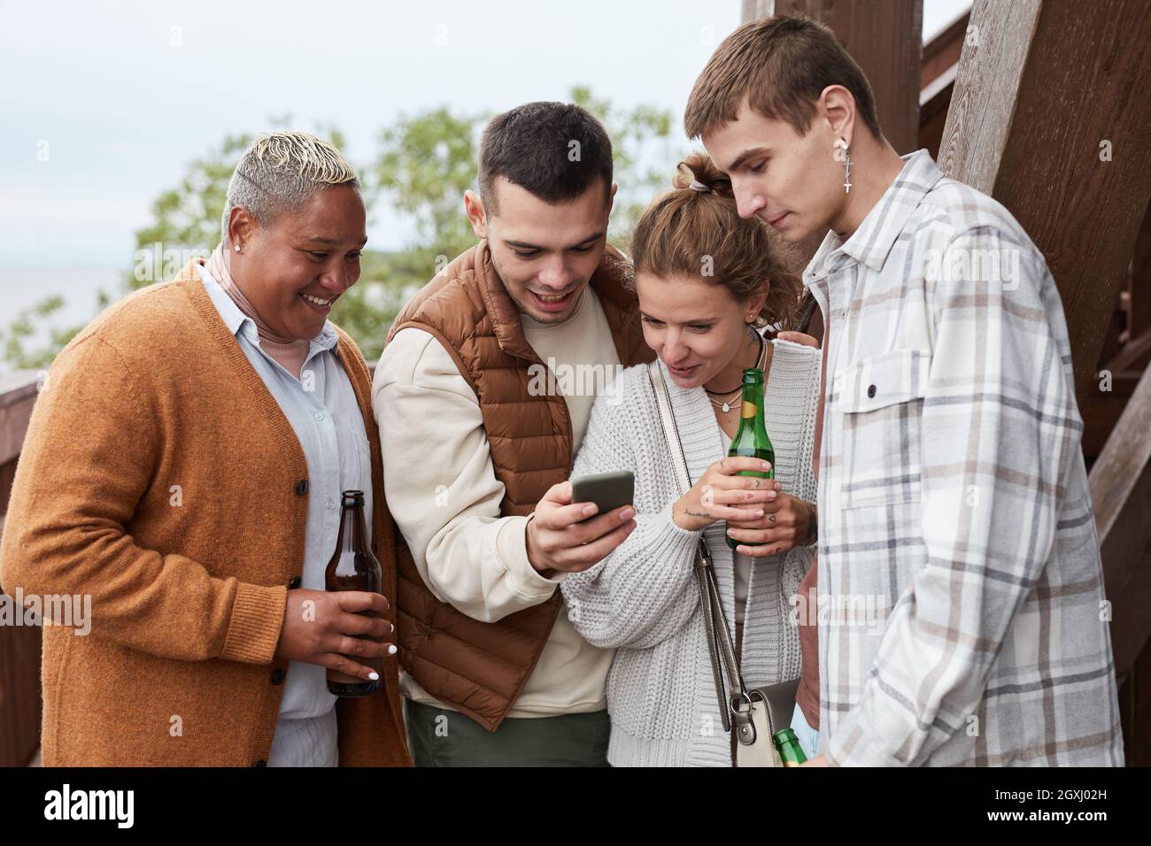 Diverse group young people using smartphone on balcony during party at lake house Stock Photo