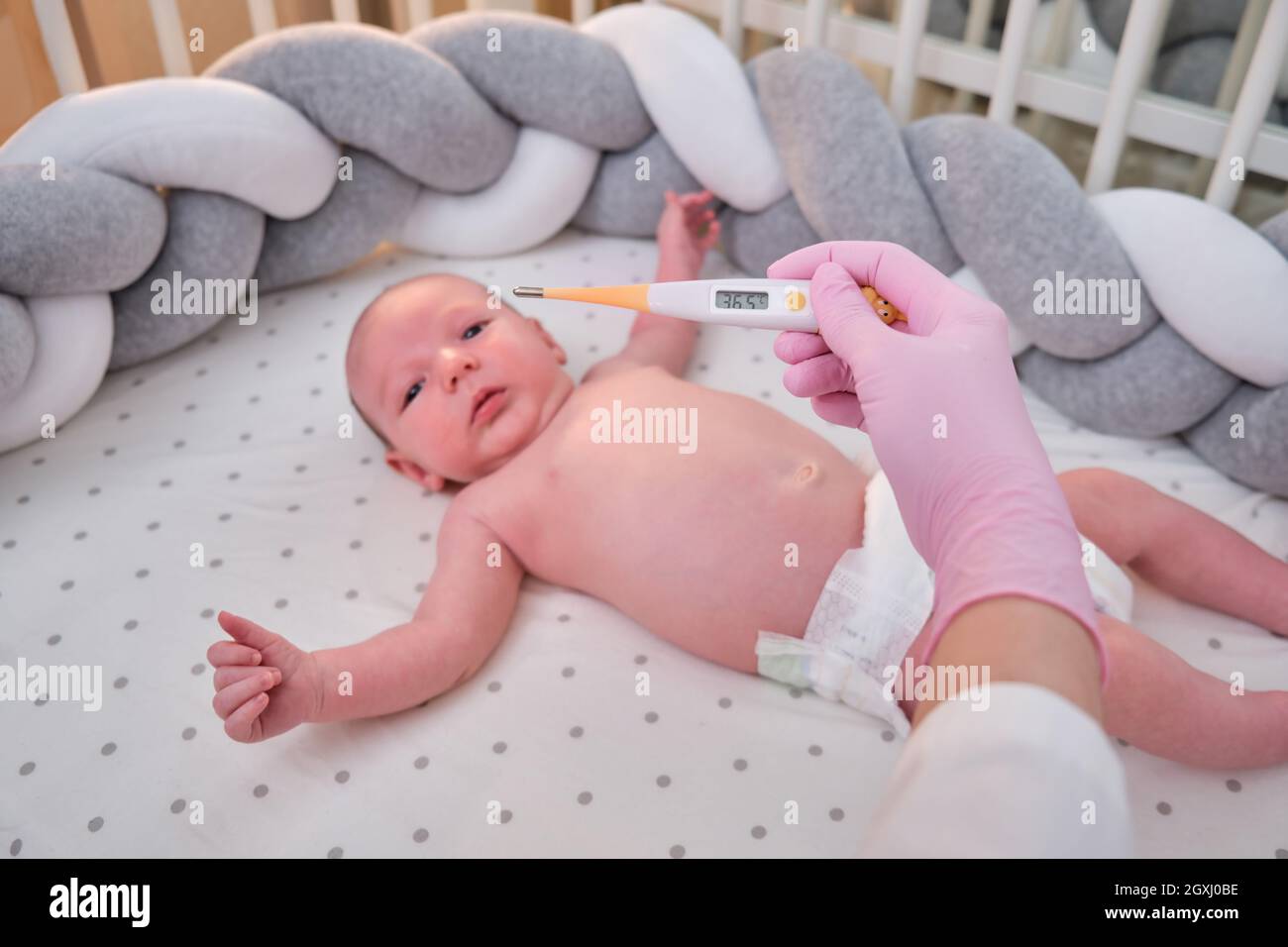 Doctor checks the temperature of the newborn baby with a thermometer. A