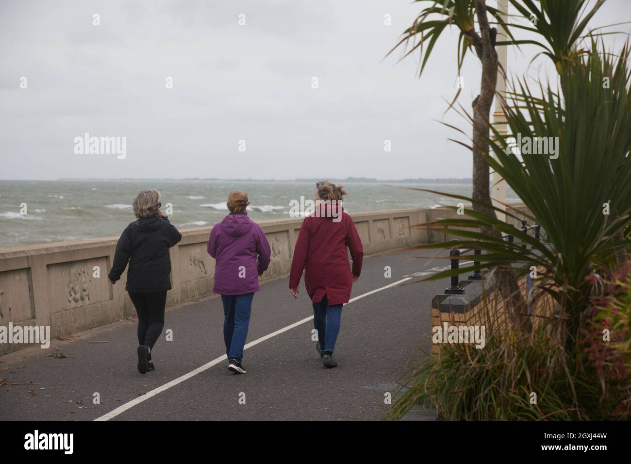 Three women seen walking along the beachfront on a windy day in autumn. Stock Photo