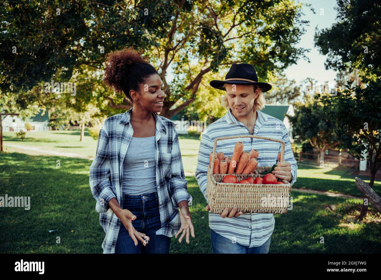 Mixed race female walking with caucasian male friend through farm village after successful vegetable picking  Stock Photo
