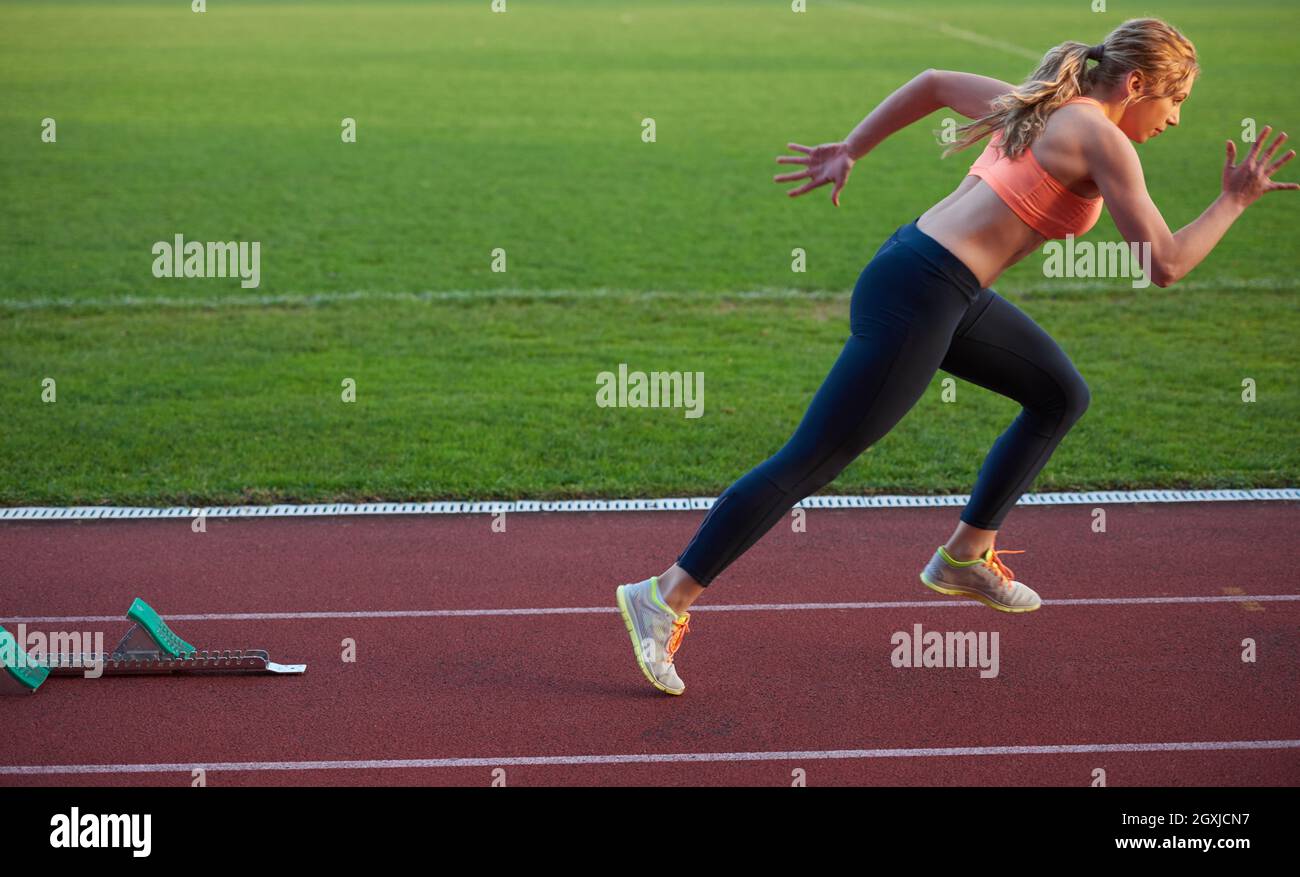 woman sprinter leaving starting blocks on the athletic track. Side view ...