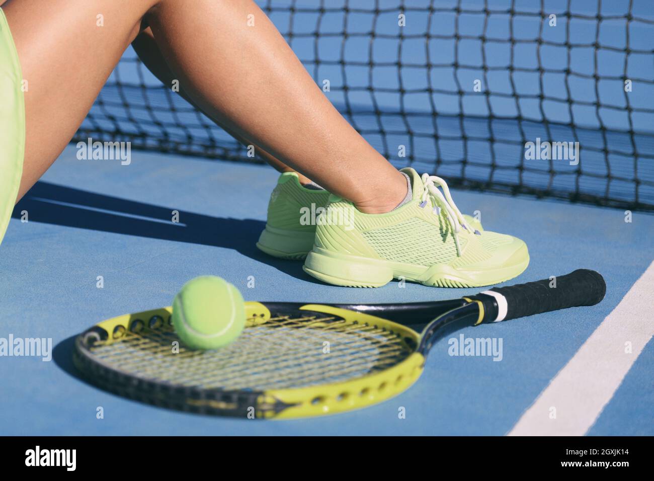 Tennis athlete player woman legs and feet wearing tennis shoes trainers. Fashion yellow activewear outfit on blue outdoor hard court. Closeup of legs Stock Photo
