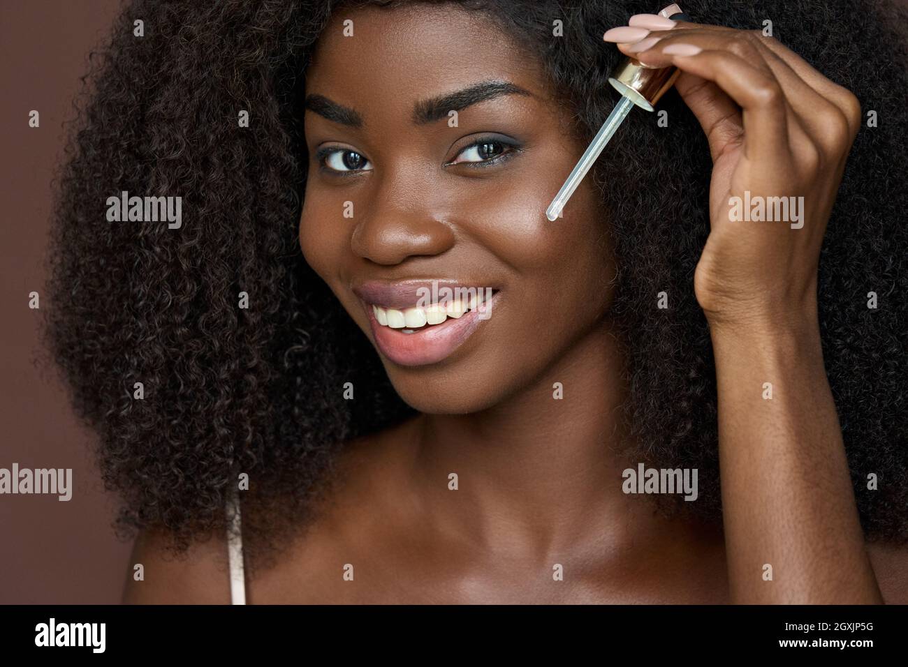 Smiling happy young African black woman applying serum oil on facial skin. Stock Photo
