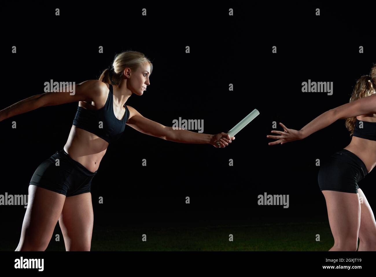 woman athletic runners passing baton in relay race Stock Photo