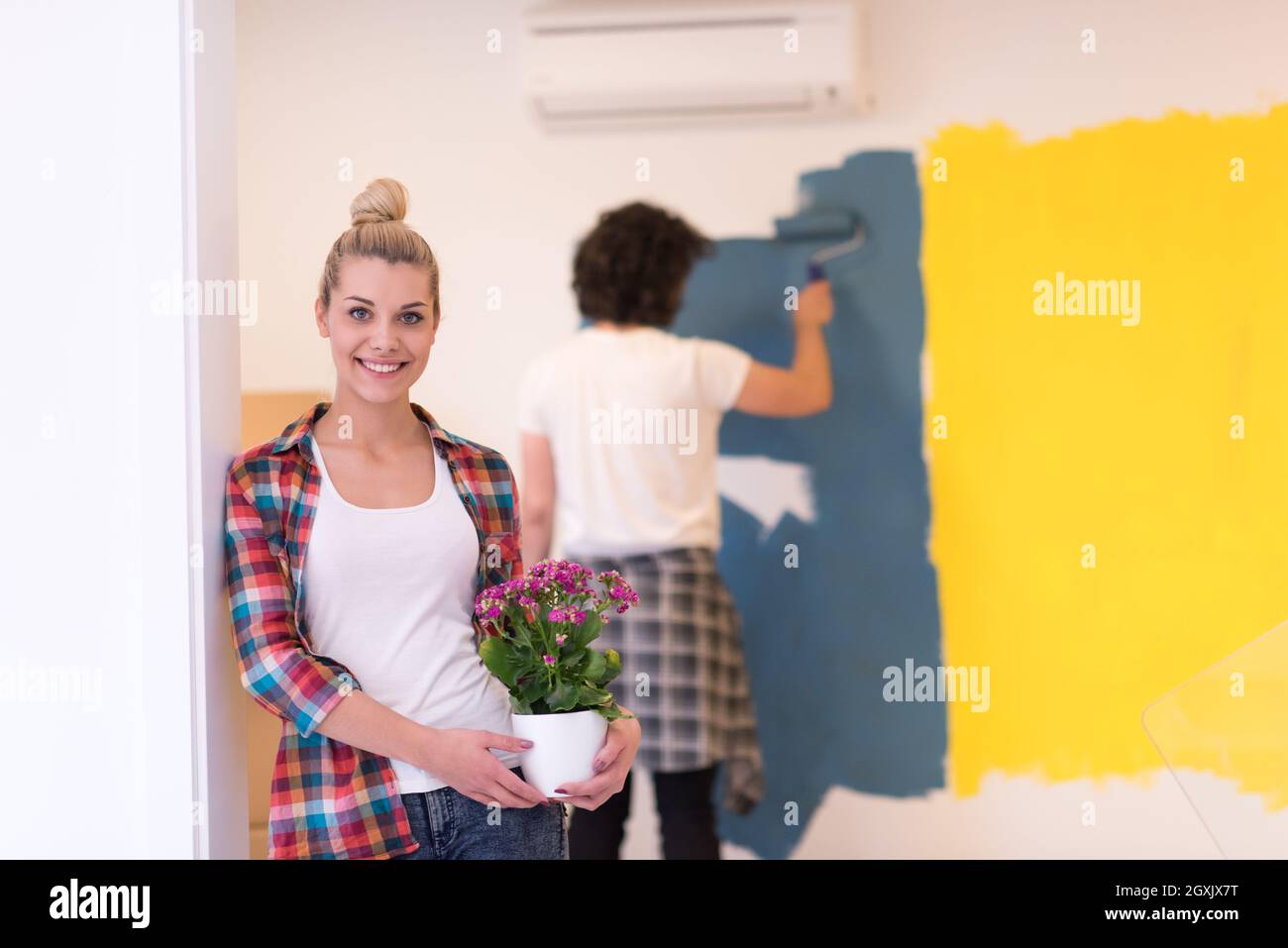 Happy couple doing home renovations, the man is painting the room and