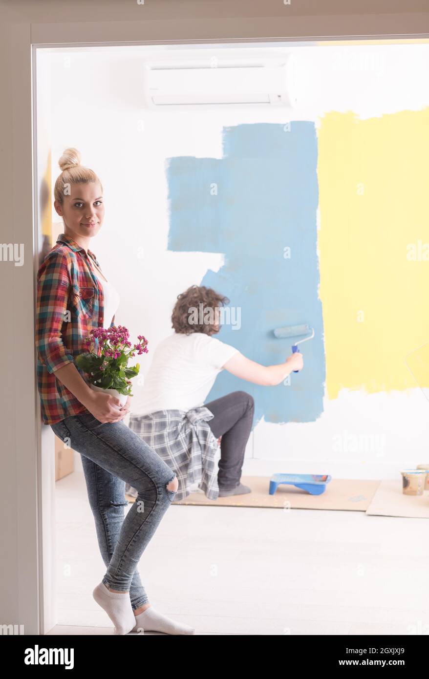 Happy couple doing home renovations, the man is painting the room and