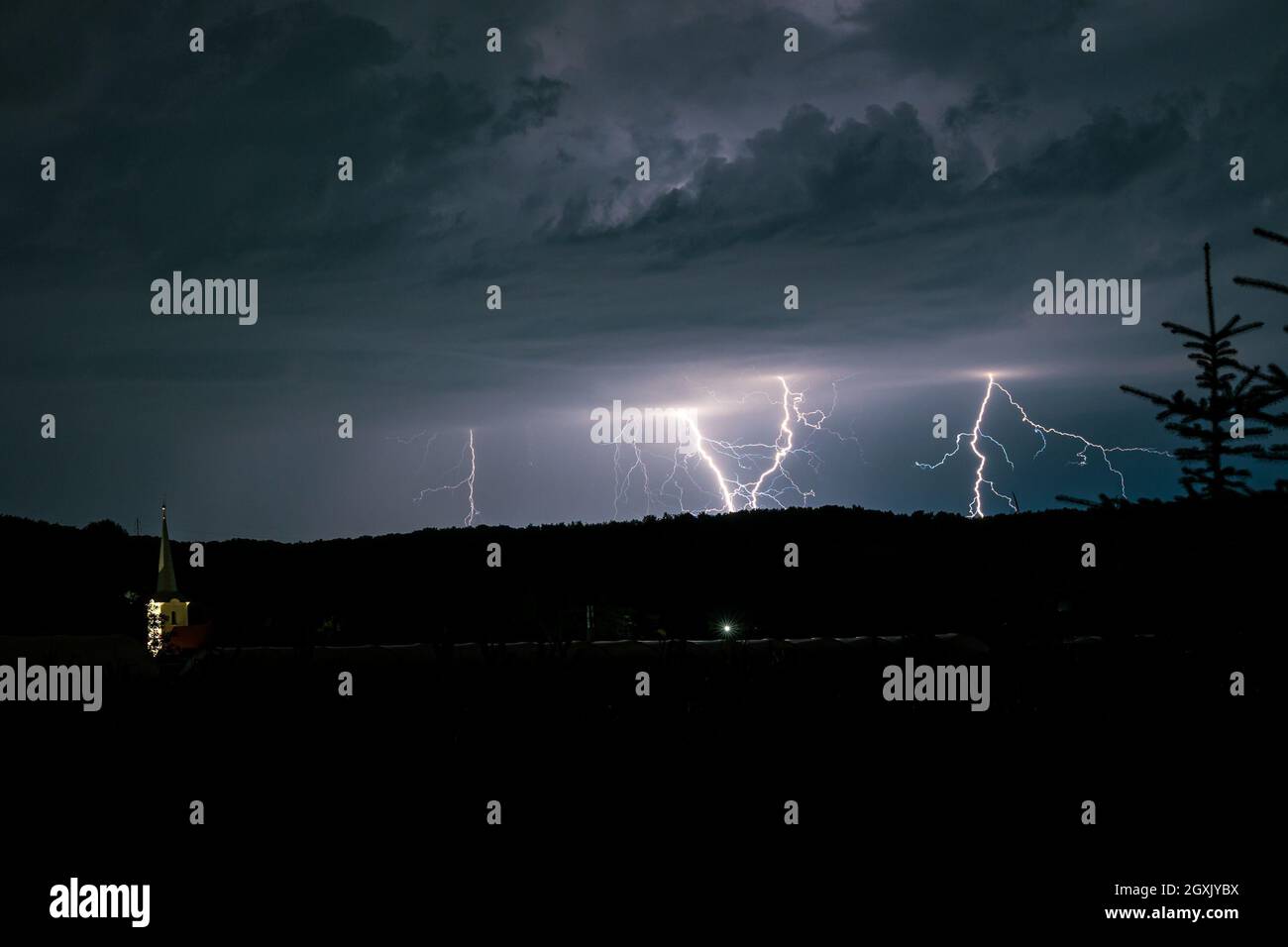 Multiple lightning bolts strike behind a hill in the landscape of Transylvania, Romania Stock Photo