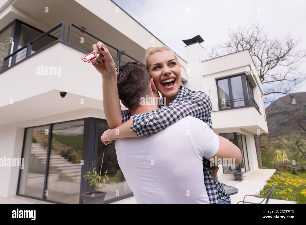 Portrait of a happy young couple hugging in front of their new luxury ...