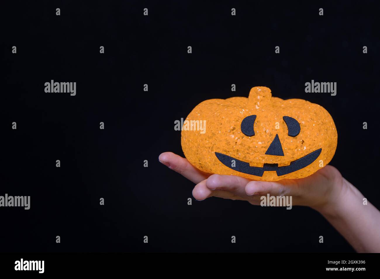 Child's hand holding orange pumpkin lantern with bared face isolated on black background. Trick or treat tradition. Happy Halloween concept Stock Photo