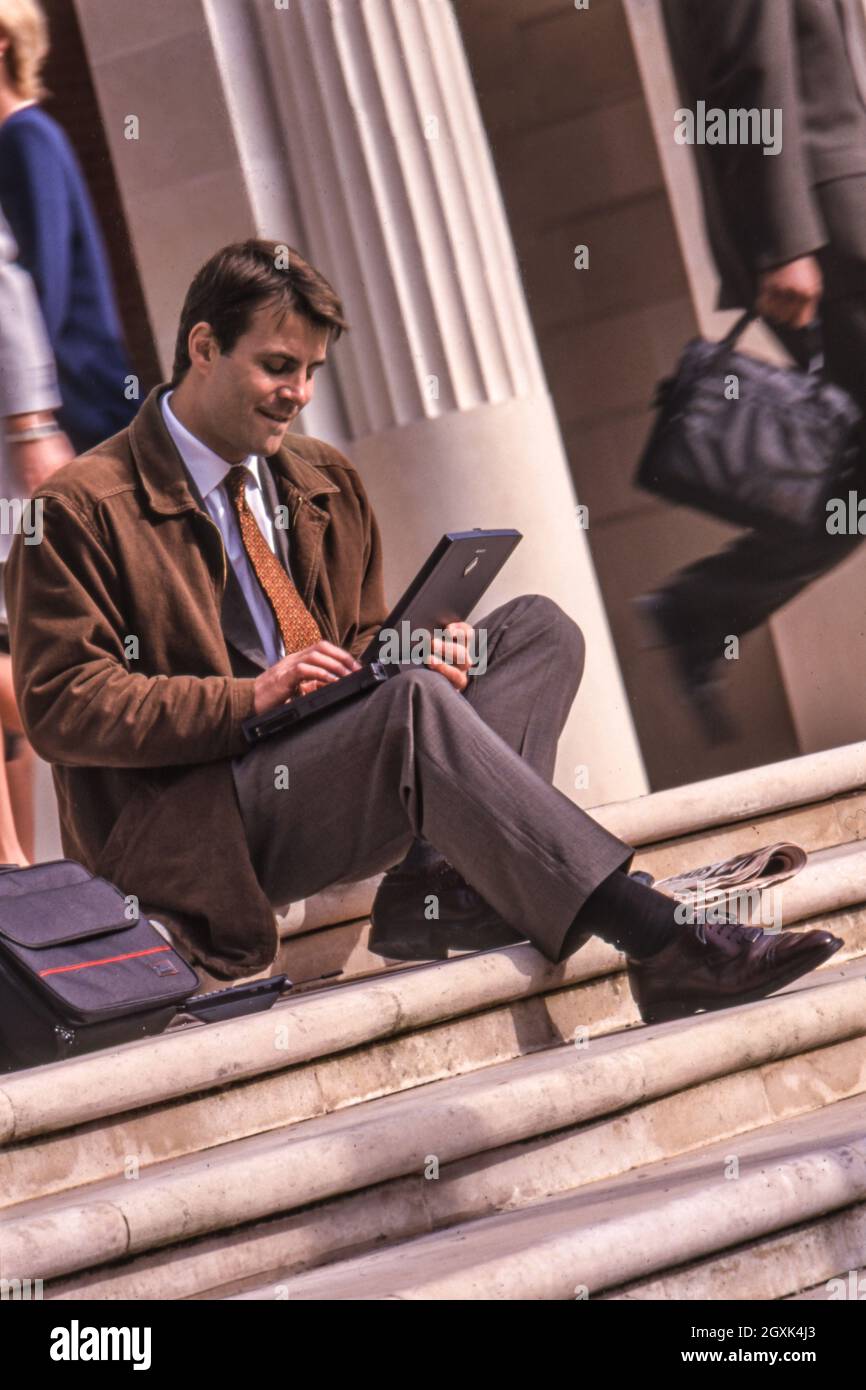 1990's Businessman with IBM ThinkPad computer sitting outside on sunny steps of busy city business environment, working on current business project. Stock Photo