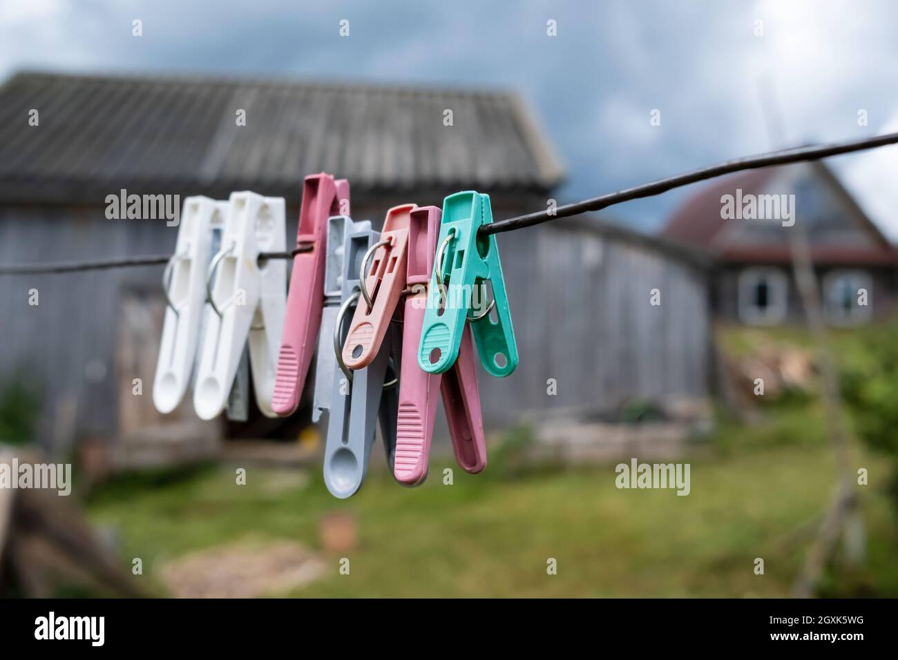 Plastic clothespins hang on clotheslines, in a rustic courtyard, against the backdrop of a wooden barn and the sky. Stock Photo